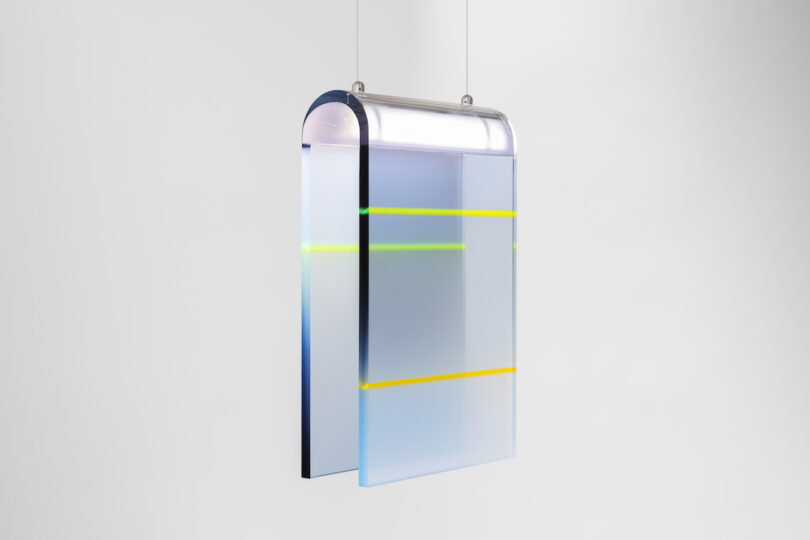 A modern rectangular pendant light with layered lucite panels featuring yellow and green accents, suspended by wires