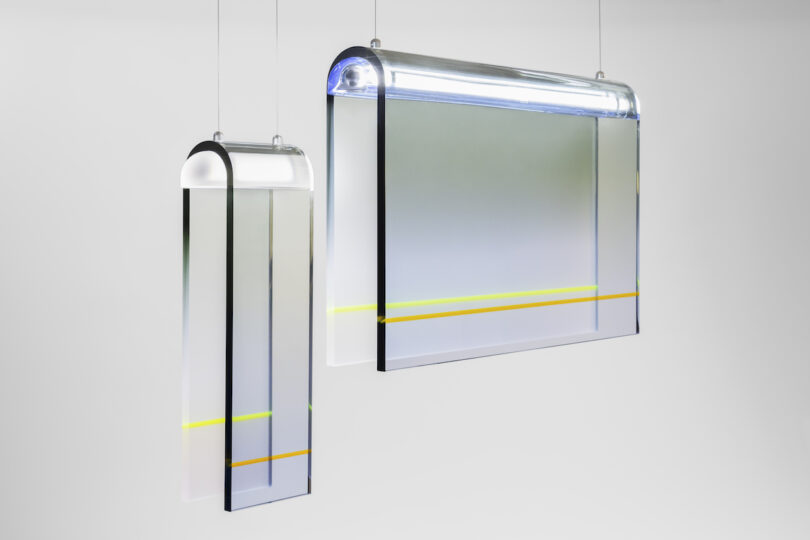 Two modern, rectangular pendant lights with clear and frosted lucite panels, featuring yellow and gray accents, suspended from thin cords in a minimalist setting