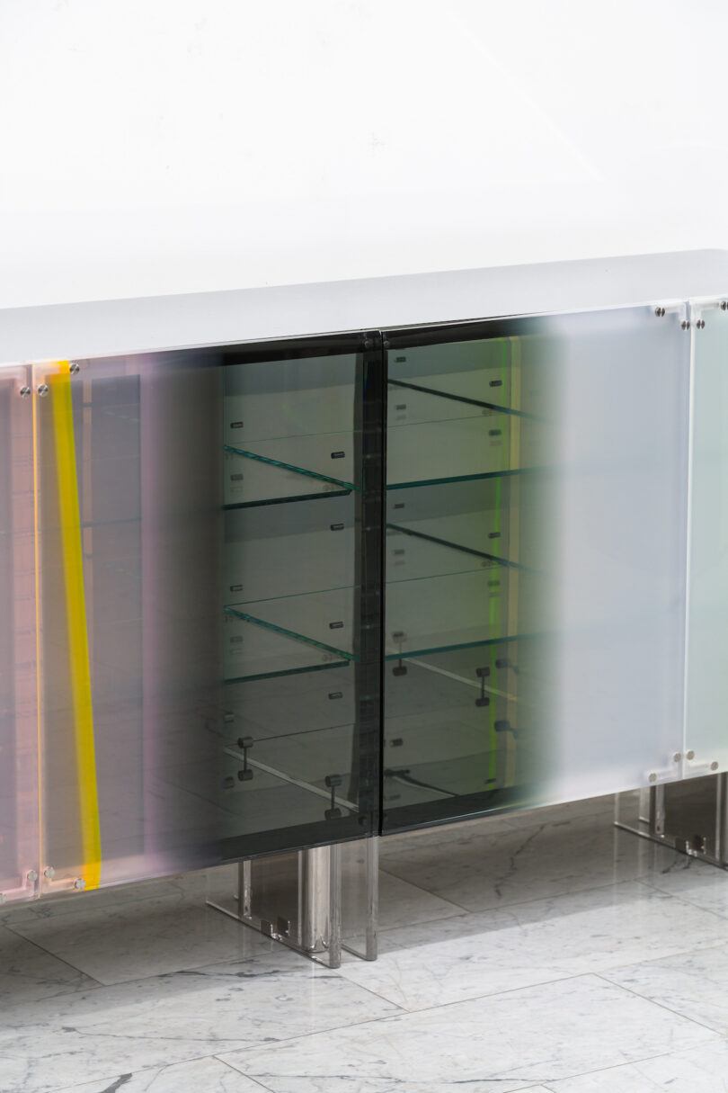 lucite sideboard with multiple shelves, featuring semi-transparent, multicolored sliding doors on a marble floor