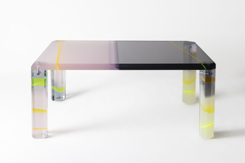 A transparent rectangular table with gradient colors from purple to black on the surface and legs featuring yellow accents