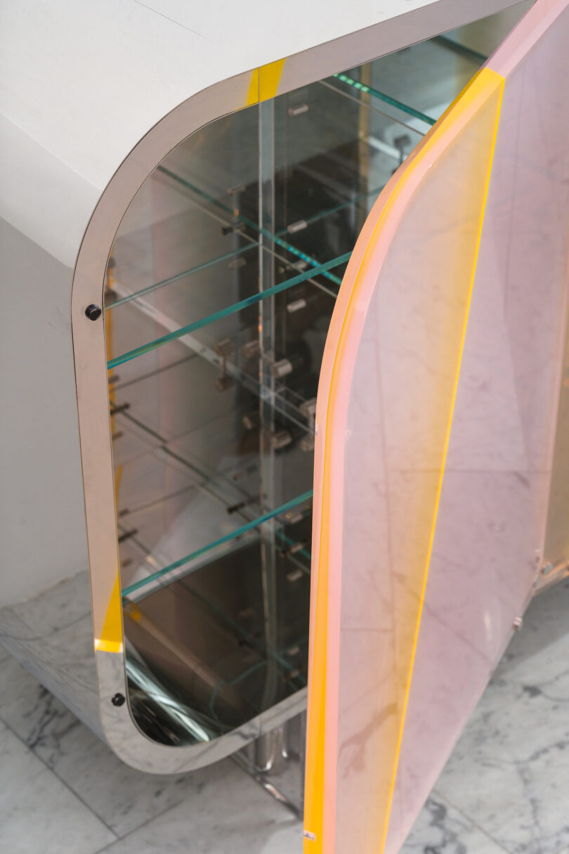 Modern lucite and metal cabinet with open doors, showcasing shelves inside, set on a marble floor.