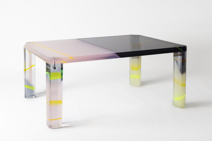 A modern, translucent table with a gradient design in shades of pink, gray, and yellow accents