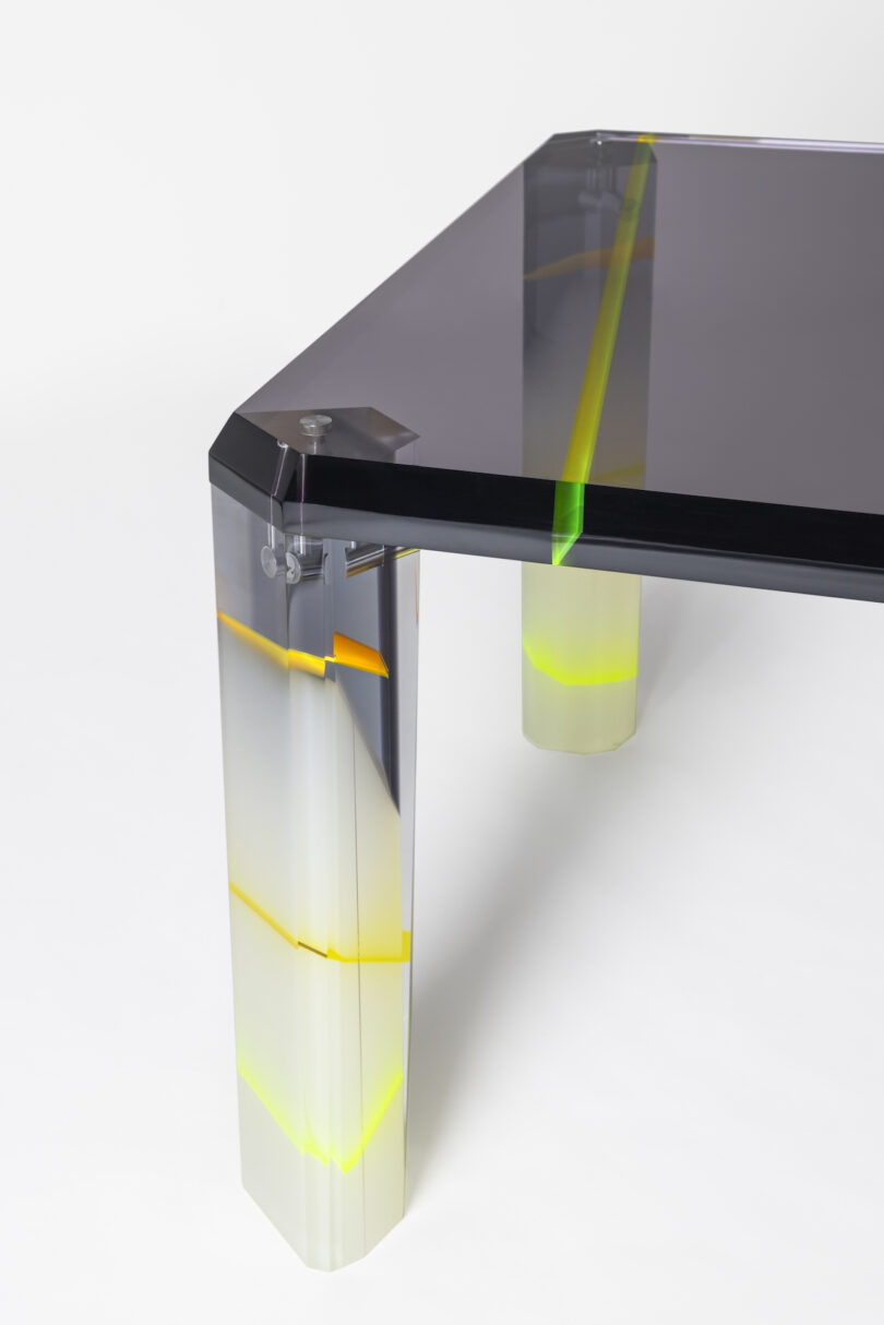 Close-up of a modern table with transparent, multi-colored legs and a dark glass top