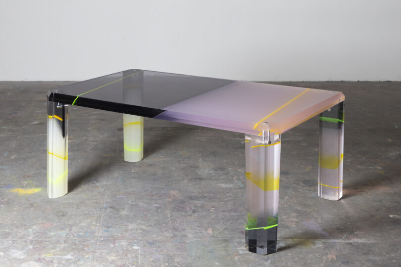 A modern, transparent table with a multicolored gradient top and legs, set against a plain background