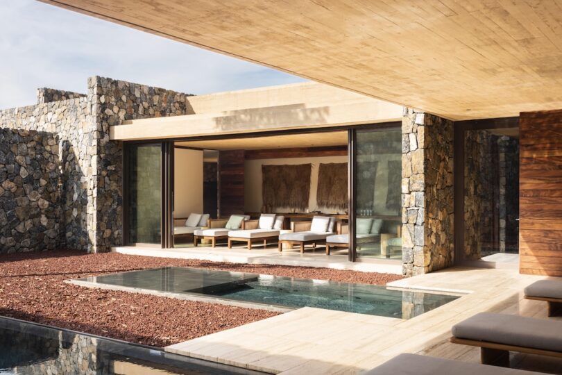 Modern outdoor patio with stone walls, large sliding glass doors, and a small reflecting pool, featuring comfortable seating and neutral colors.