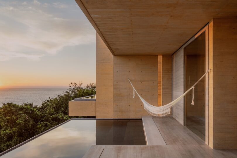 Modern concrete building with a hammock on the patio overlooking the ocean at sunset.