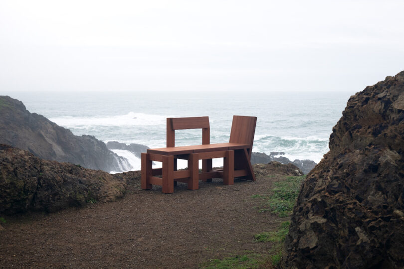 A wooden table and chair set placed on a rocky cliffside overlooking the ocean on a cloudy day