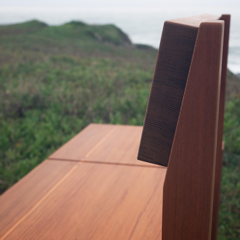 Close-up of a wooden bench with a view of a grassy hillside and the sea in the background