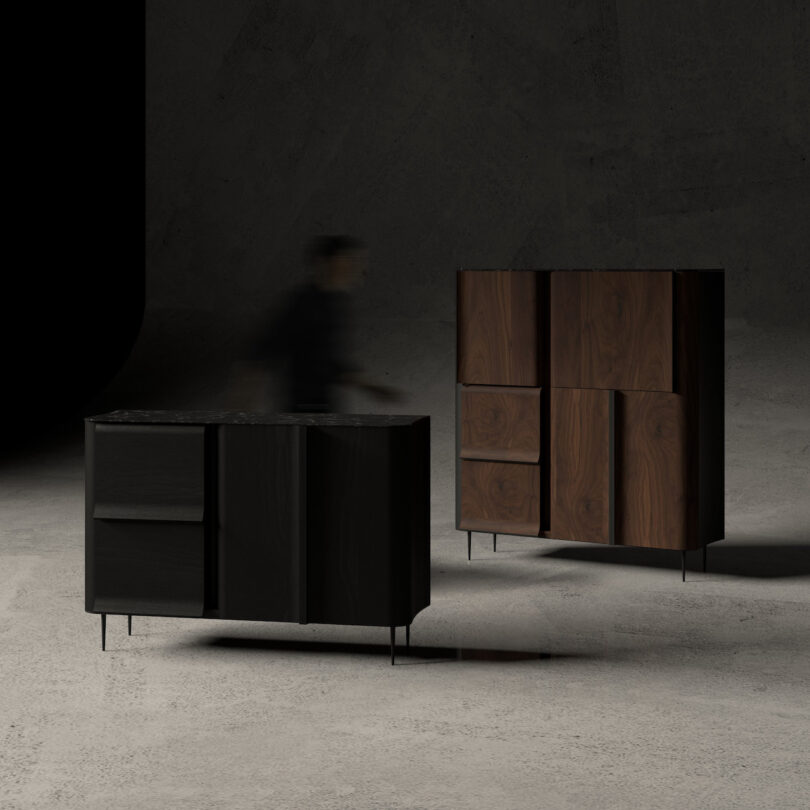 A person moves between two modern cabinets with a dark, minimalist design on a concrete floor