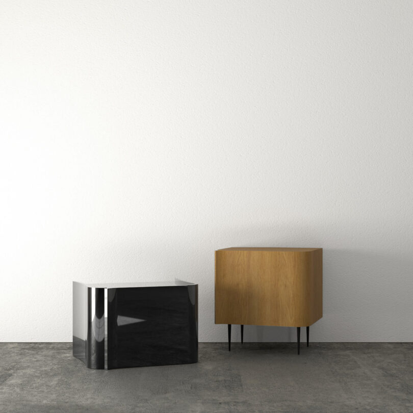 A wooden cabinet with black legs and a shiny black cube are placed on a concrete floor against a white wall