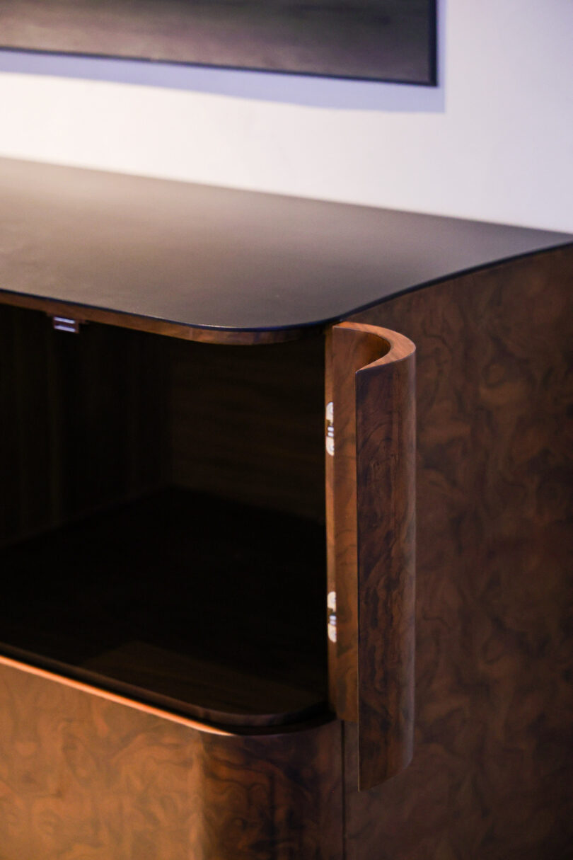 A dark wooden cabinet with a rounded corner and an open door is set against a white wall