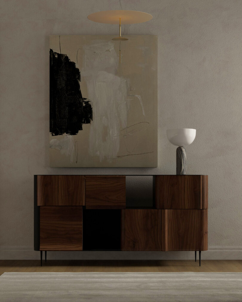 A modern sideboard with a geometric design stands against a beige wall. Above it hangs an abstract painting in black and white. 