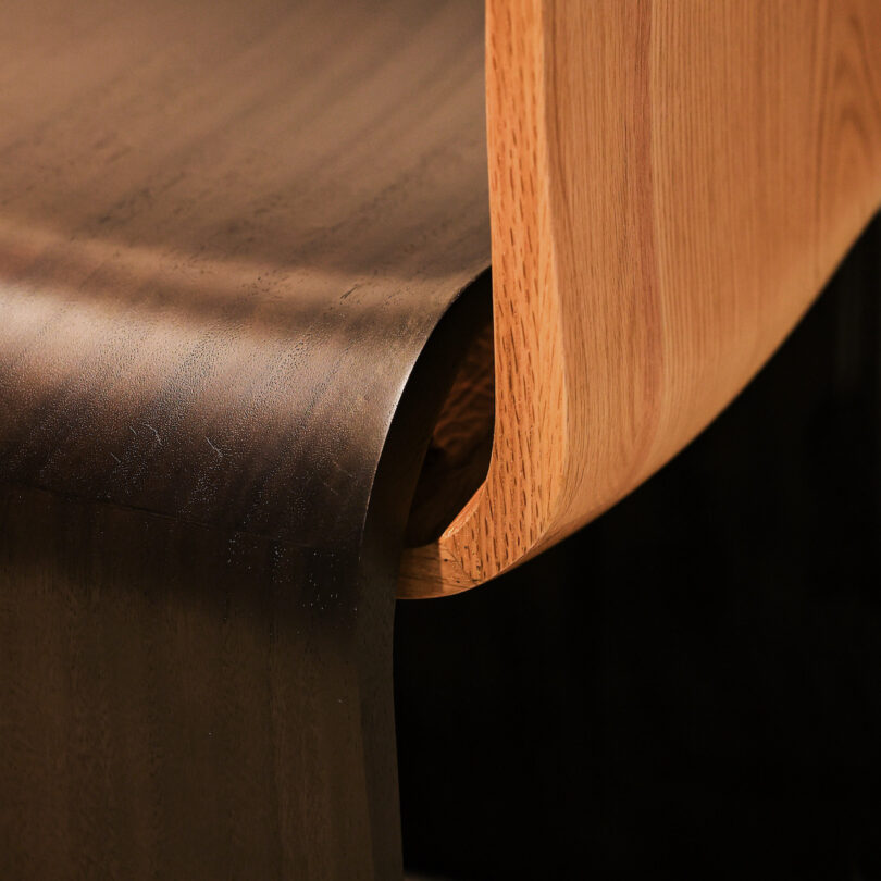 Close-up of a wooden chair showing a contrast between light and dark wood tones with a smooth, curved design