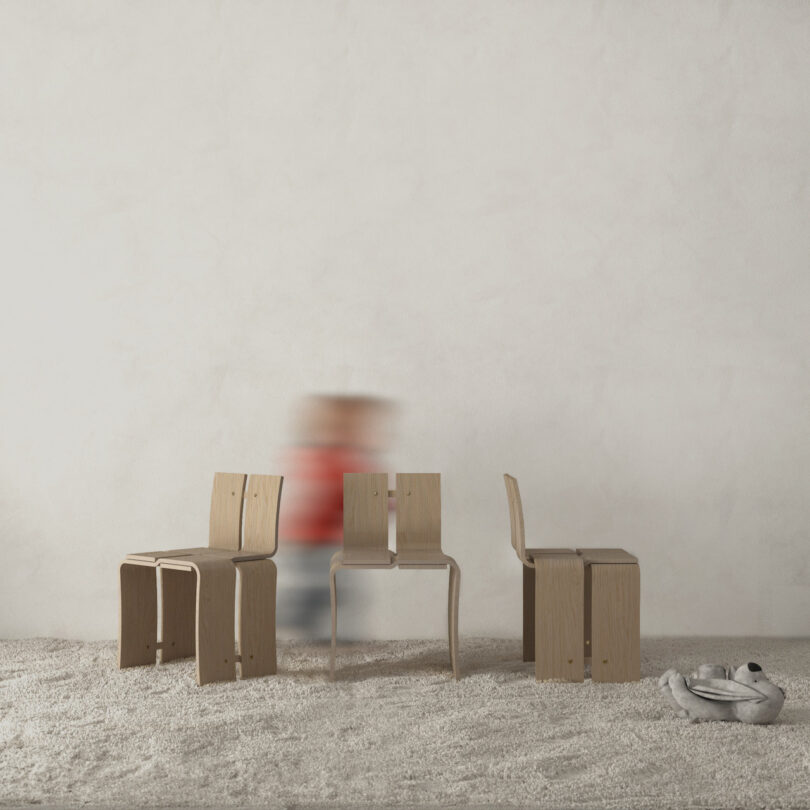 Three wooden chairs on a carpet with a blurred person in a red shirt in the background and a silver kettlebell on the floor