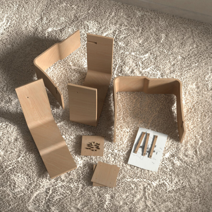 Disassembled wooden furniture pieces on a carpet, including panels, a small square piece, screws, and instructions