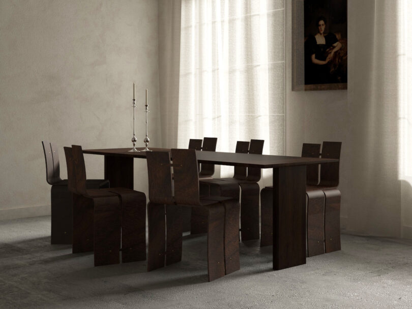 A minimalist dining room features a dark wood table and chairs on a light carpet. Two candlesticks are on the table, and a portrait hangs on the wall near sheer curtains