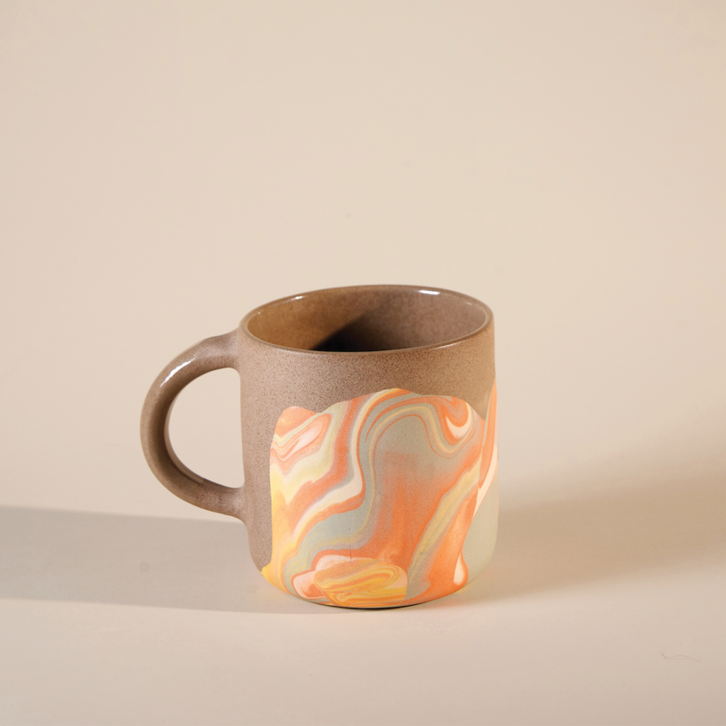 A ceramic mug with a swirling orange, yellow, and gray pattern, placed on a plain background