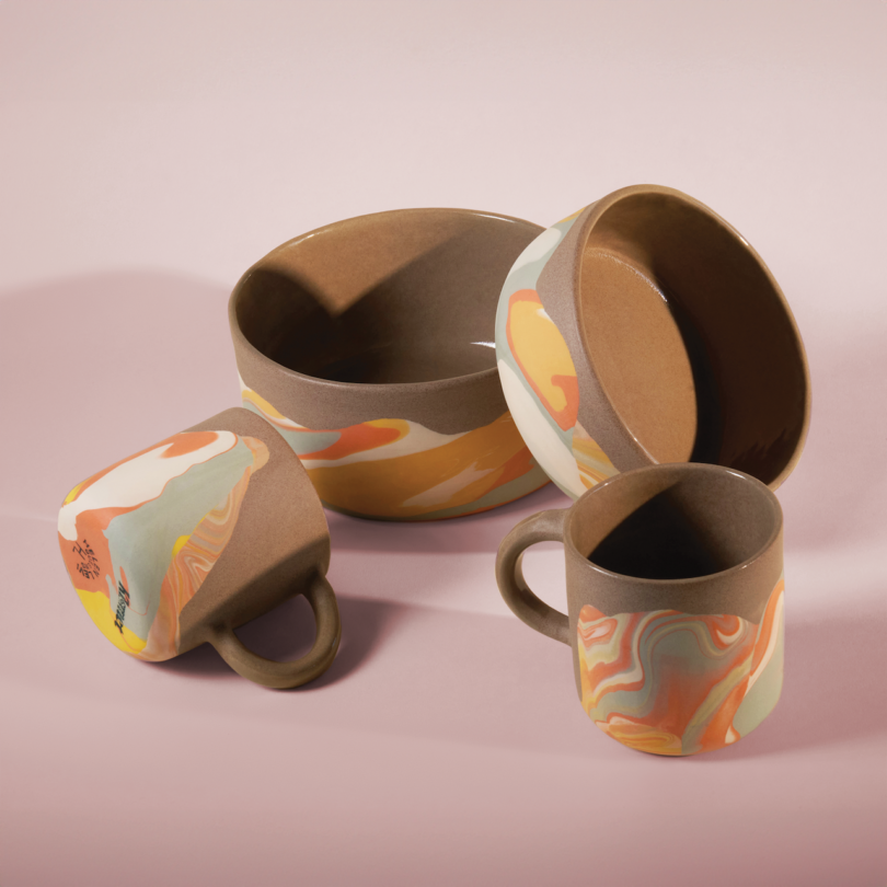 Ceramic bowls and mugs with colorful, abstract patterns placed on a light pink background