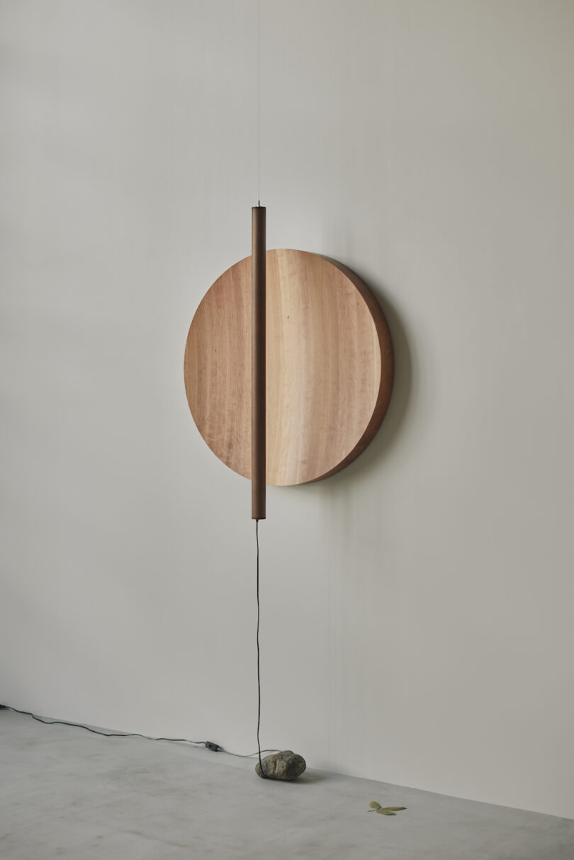 A modern wall lamp with a round wooden backplate and vertical cylindrical light, mounted on a light-colored wall