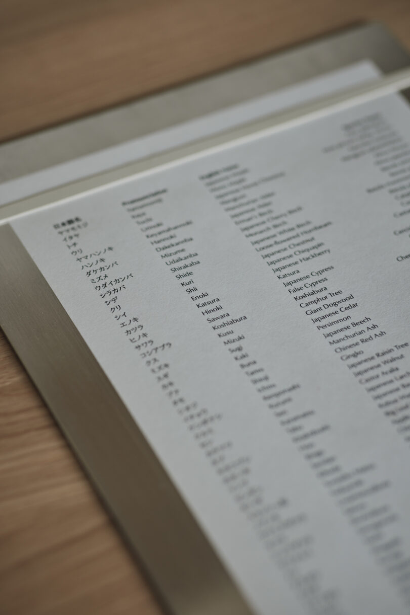 A close-up of a printed cocktail menu in a metal frame on a wooden table, featuring a list of drink names in English and Japanese