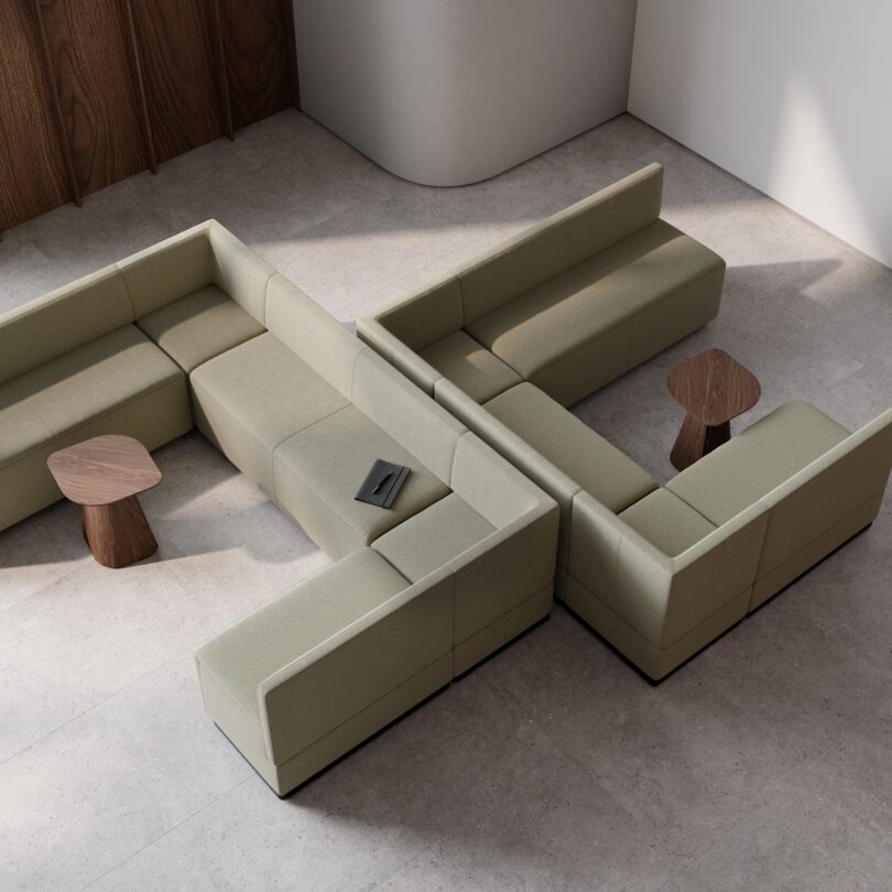 Aerial view of a modular L-shaped olive green sofa with a book on one section. Two wooden side tables are placed nearby on a light stone floor