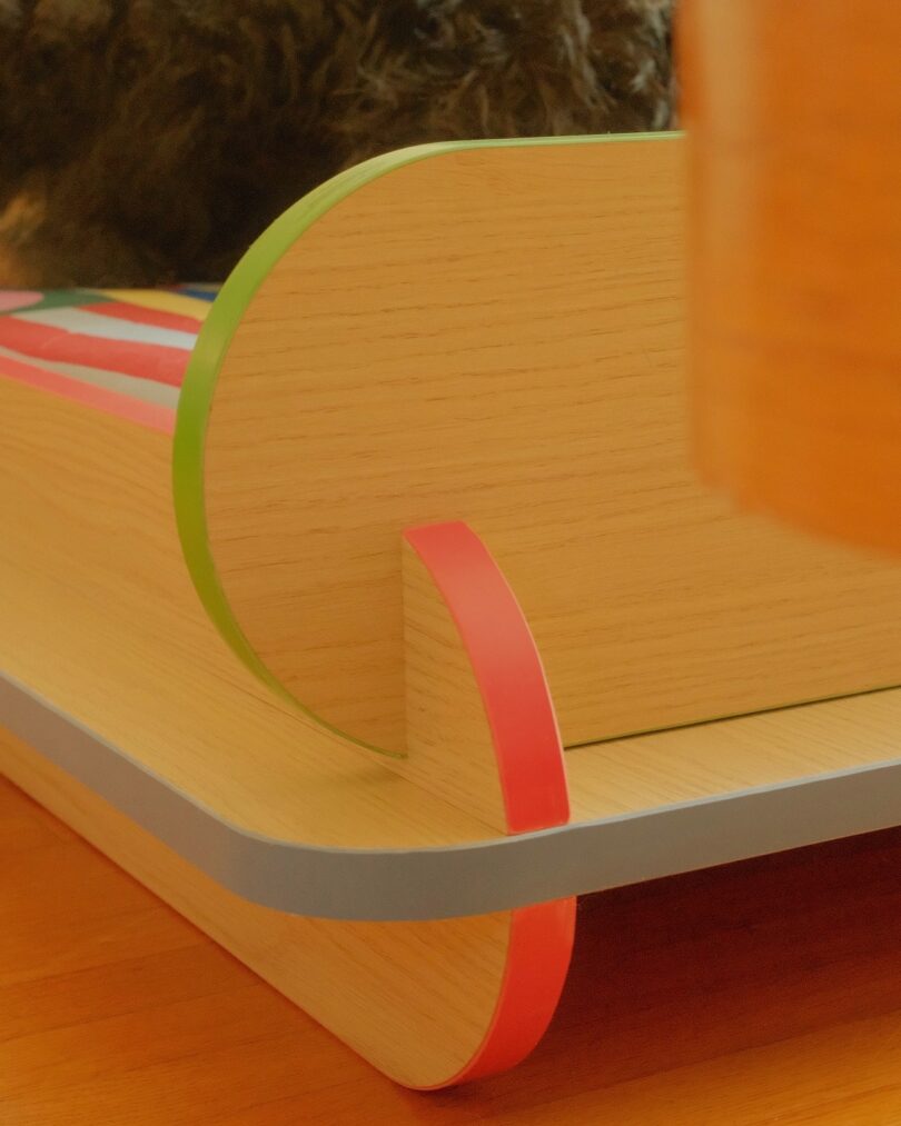 Close-up of a wooden furniture piece with rounded edges, featuring red and green accents, placed on a wooden floor