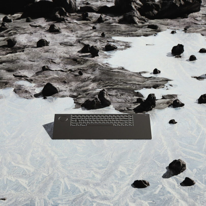 A black keyboard lies on a rocky, icy surface; rocks scattered around.