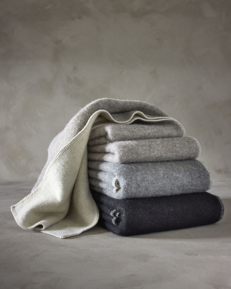 A neatly folded stack of five wool blankets in varying shades of gray is displayed against a neutral background