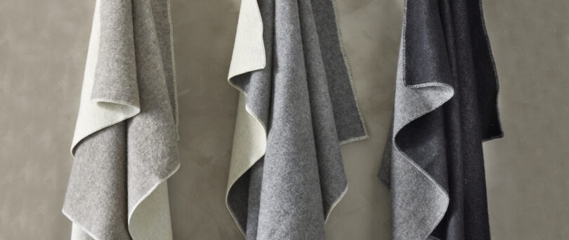 Three woolen blankets in light gray, medium gray, and dark gray hang on a wall