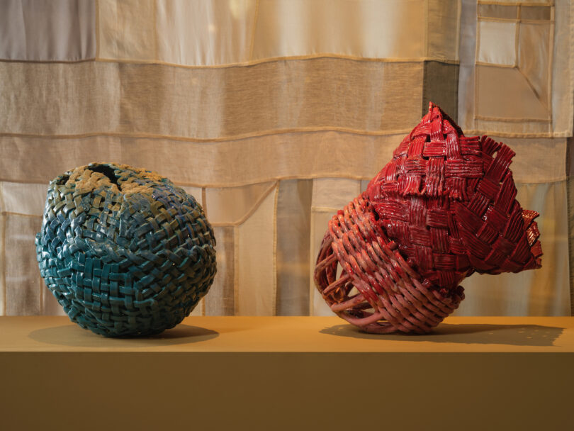 Two woven baskets, one blue and one red, displayed on a table against a textured beige backdrop