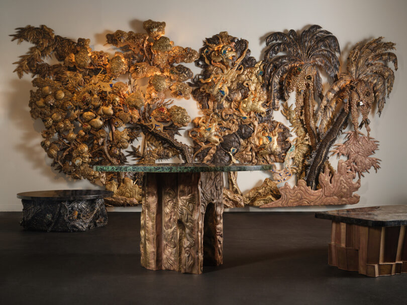 A room features ornate, nature-themed wooden sculptures and furniture, including a table and decorative wall panels with trees and leaves