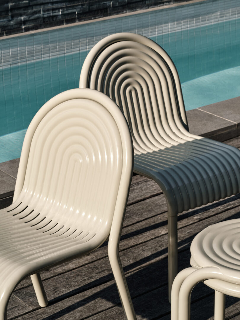 Two beige, ripple-patterned chairs next to a turquoise pool, with shadows cast on a wooden deck