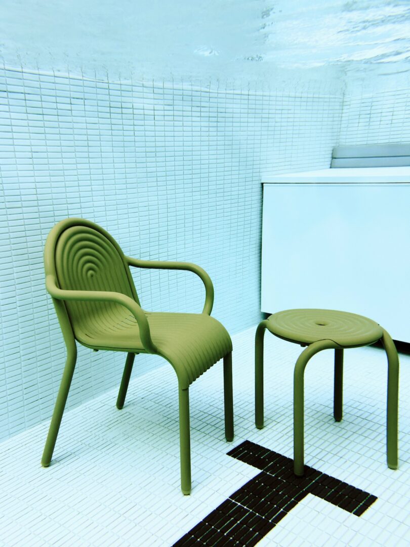 Green chair and matching stool submerged underwater in a tiled pool