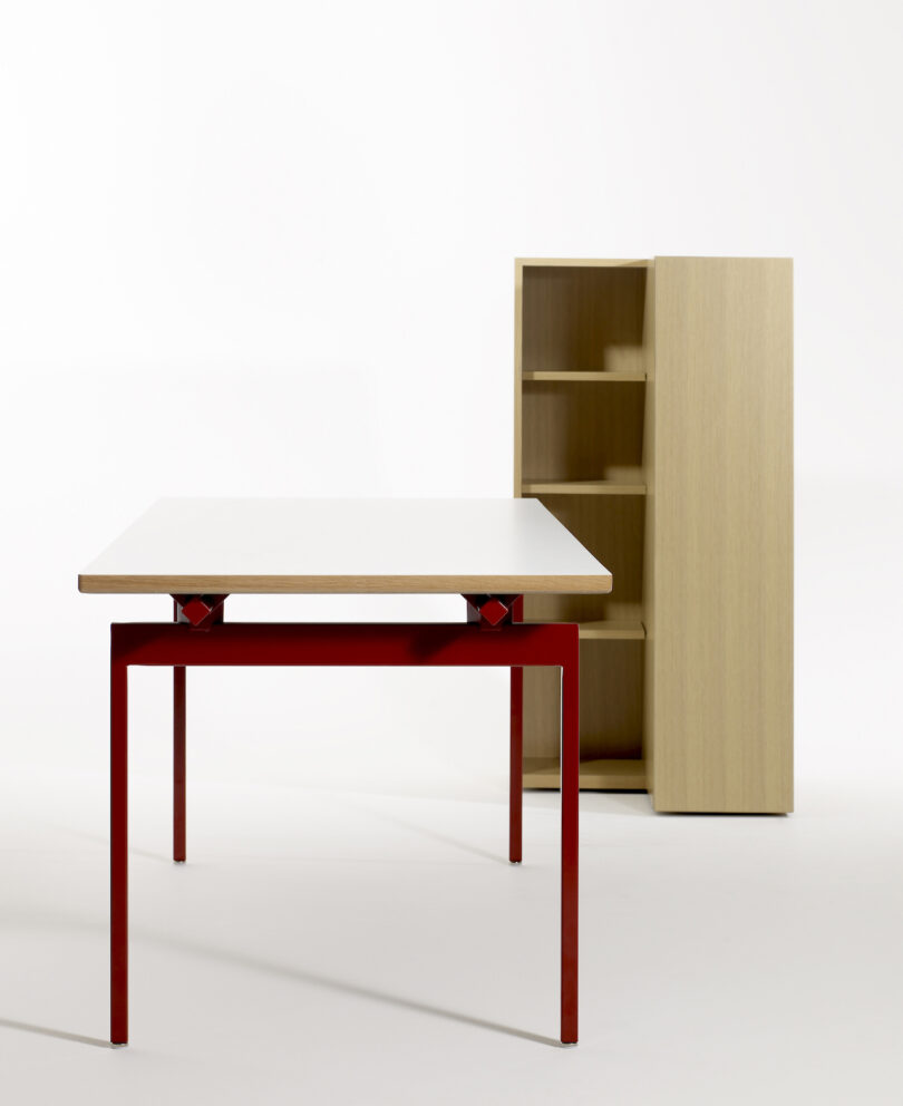 Wooden table with red legs and a matching open shelf unit in the background, set against a plain white background