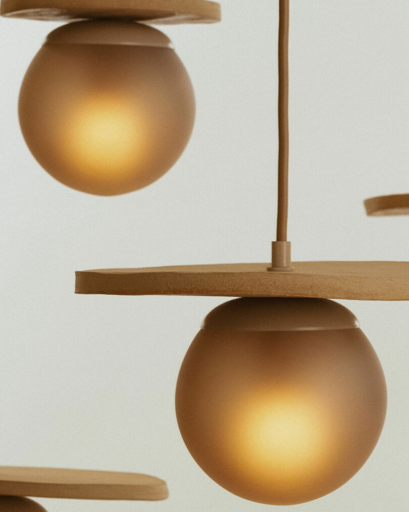 Close-up of two spherical pendant lights with warm yellow glow, hanging from brown cords, against a beige background