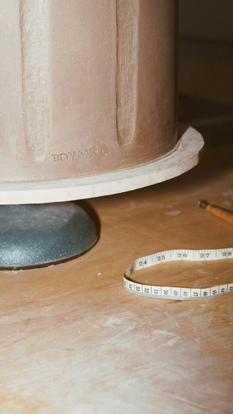 Close-up of a ceramic object, a measuring tape, and a pencil on a wooden surface