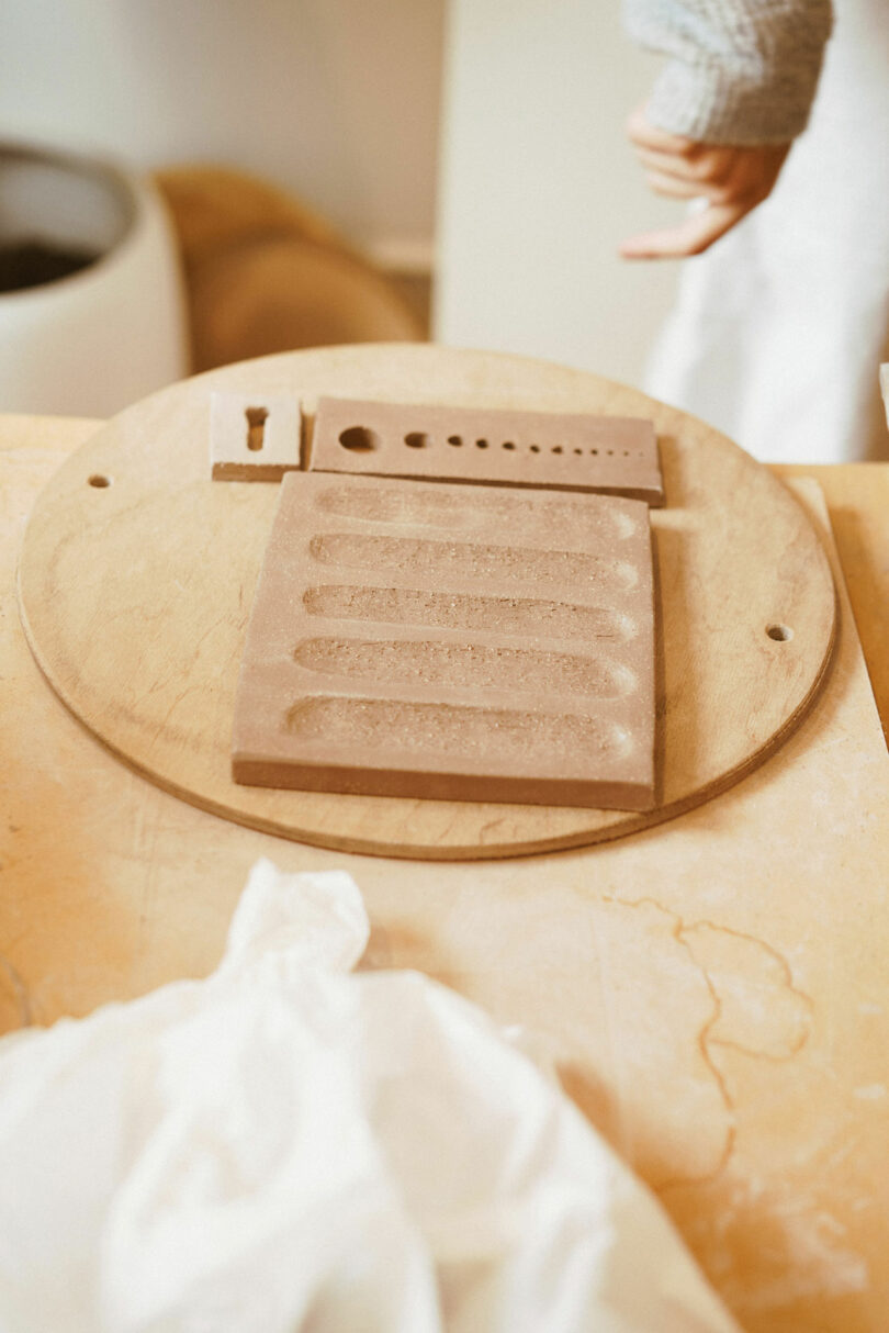 Clay slab with indentations and cutouts on a wooden board in a workshop setting