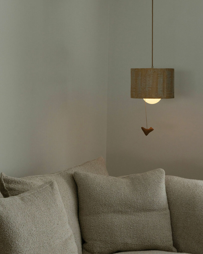 Cozy corner with beige textured couch and cushions next to a hanging pendant light with a fabric shade, against a plain wall