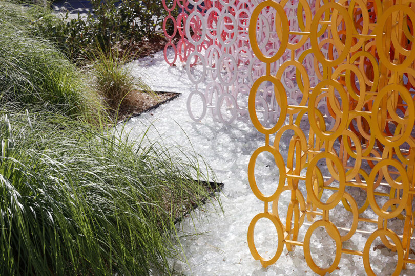 Vibrant yellow and pink circular metal structures with lush green grass on a white gravel base.