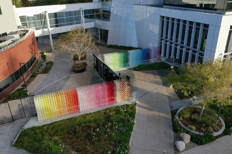 A colorful, circular-patterned wall installation outside a modern building, with trees and greenery nearby.