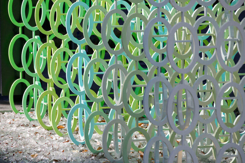 A structure of overlapping green and blue circular patterns with scattered leaves on the ground showcases the vibrant essence of 100 Colors by Emmanuelle Moureaux.