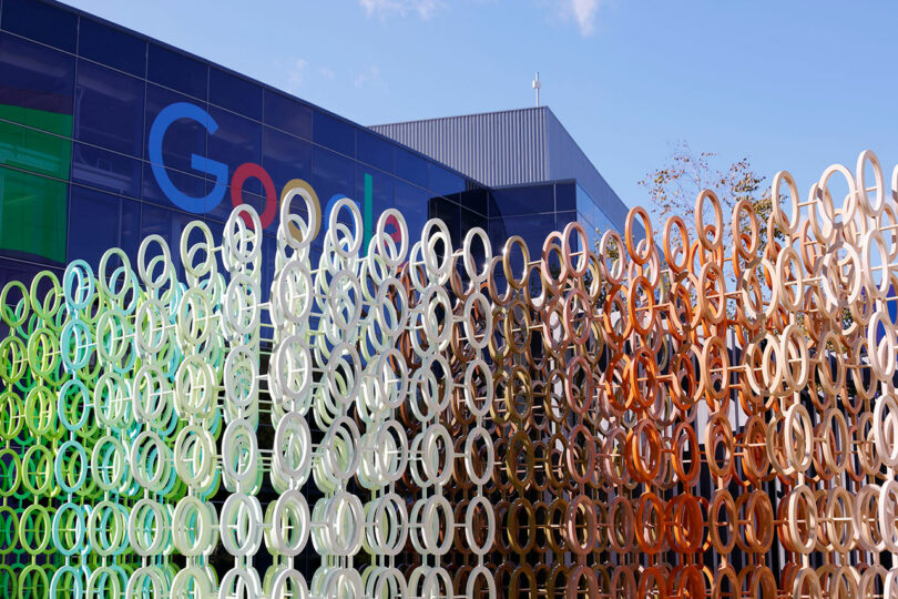 A vibrant sculpture titled "100 Colors" by Emmanuelle Moureaux stands proudly in front of a modern building, adorned with the iconic Google logo.