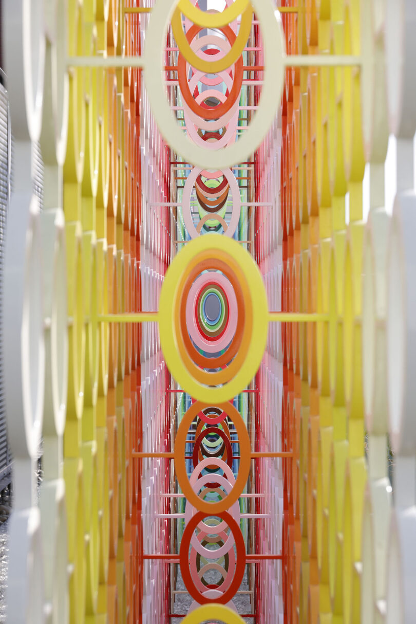 View through a colorful installation composed of concentric circles in shades of yellow, orange, and pink, arranged in a symmetrical, tunnel-like formation.