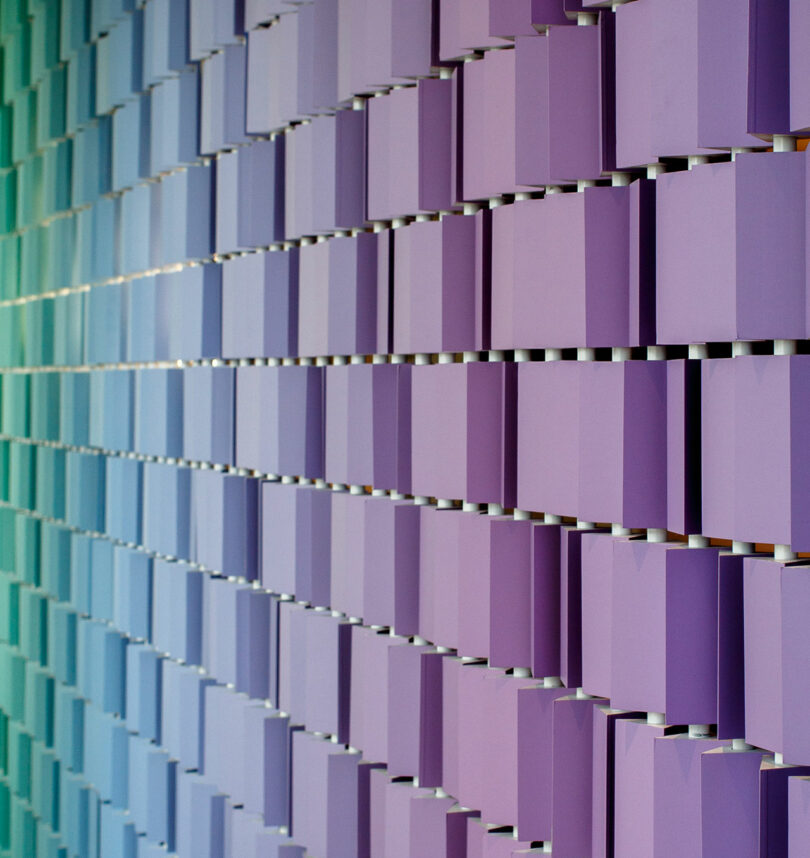 A wall covered with staggered, vertical panels in a gradient of pastel colors ranging from green to purple.