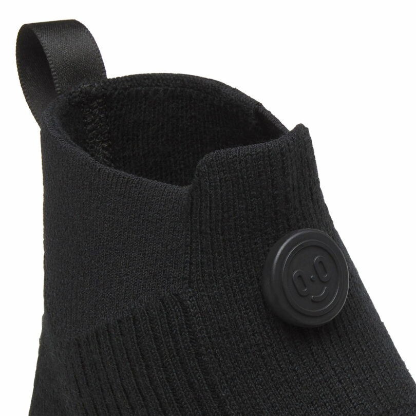 Close-up of a black knitted shoe with a smiley face button on the side.