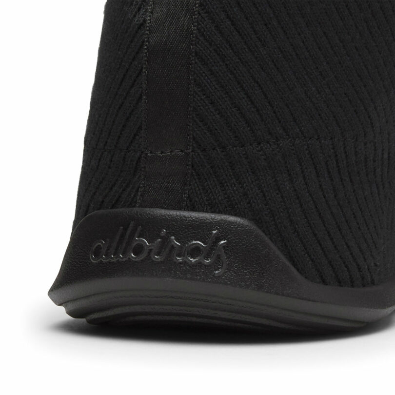 Close-up of a black shoe heel with textured fabric and "allbirds" embossed on the sole.