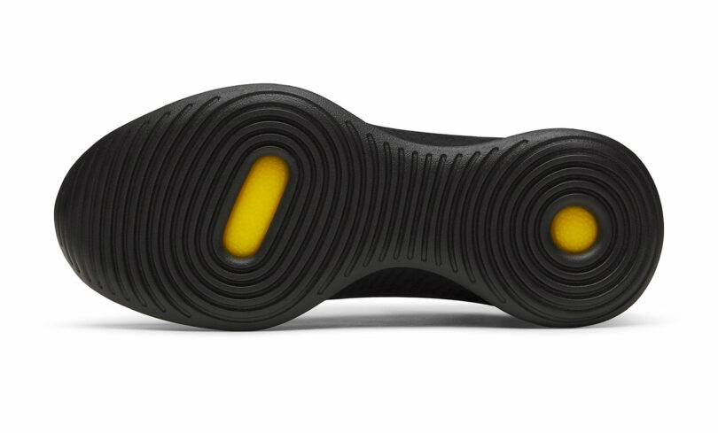 Black shoe sole with circular grooves, featuring two visible yellow cushioning areas.