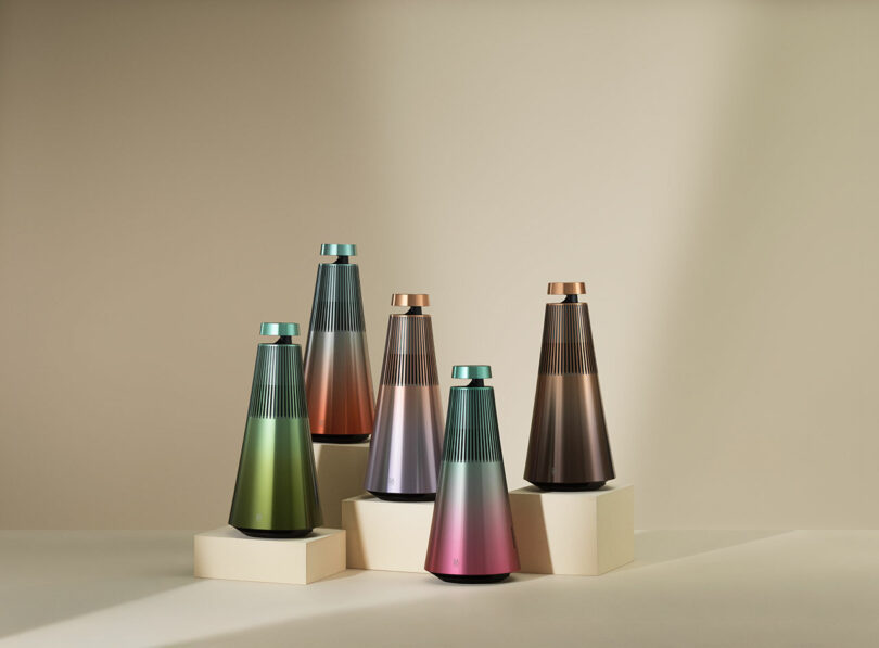 Five conical Bang & Olufsen speakers with gradient colors are displayed on beige platforms against a neutral background.