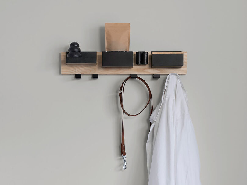 Biting Edge design meets functionality in this wooden wall shelf, featuring sleek black compartments for your items. A white shirt and a brown leather strap stylishly hang from the hooks below.