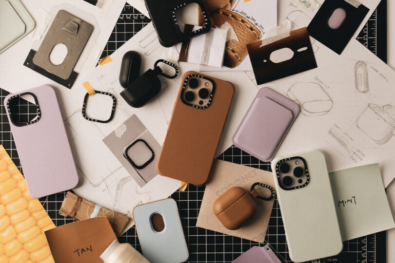 Various smartphone cases and accessories in different colors and materials are scattered on a table with design sketches and fabric samples.